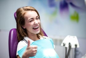 A dentist patient giving a thumbs-up, smiling and winking.