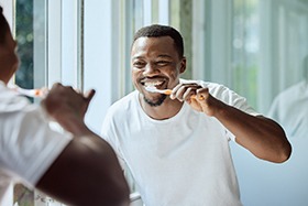 Man smiling while brushing teeth in bathroom