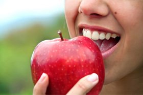 Woman with dental implants in Dallas, TX about to bite an apple 