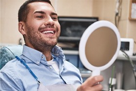 Male dental patient with dental implants in Dallas, TX looking in a handheld mirror