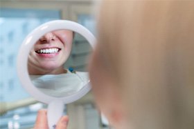 Dental patient holding mirror, looking at her new smile