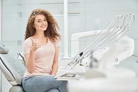 Woman in light pink shirt giving thumbs up in dental chair
