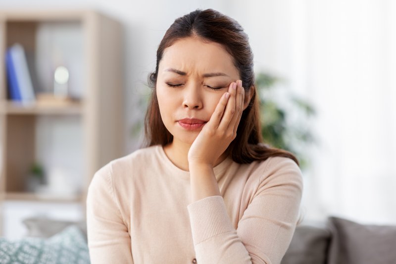 person holding their tooth and wincing in pain